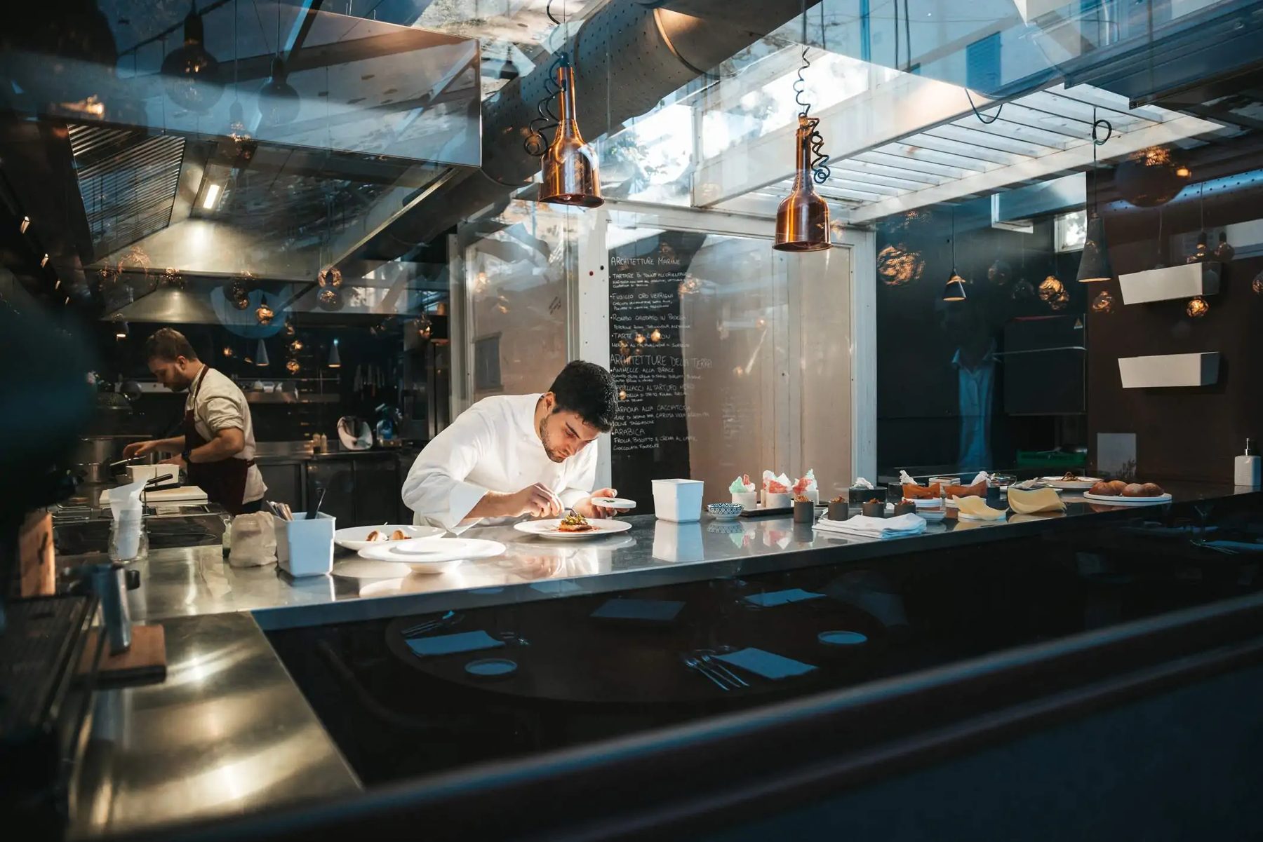 A chef plating a dish at the pass of an open restaurant kitchen
